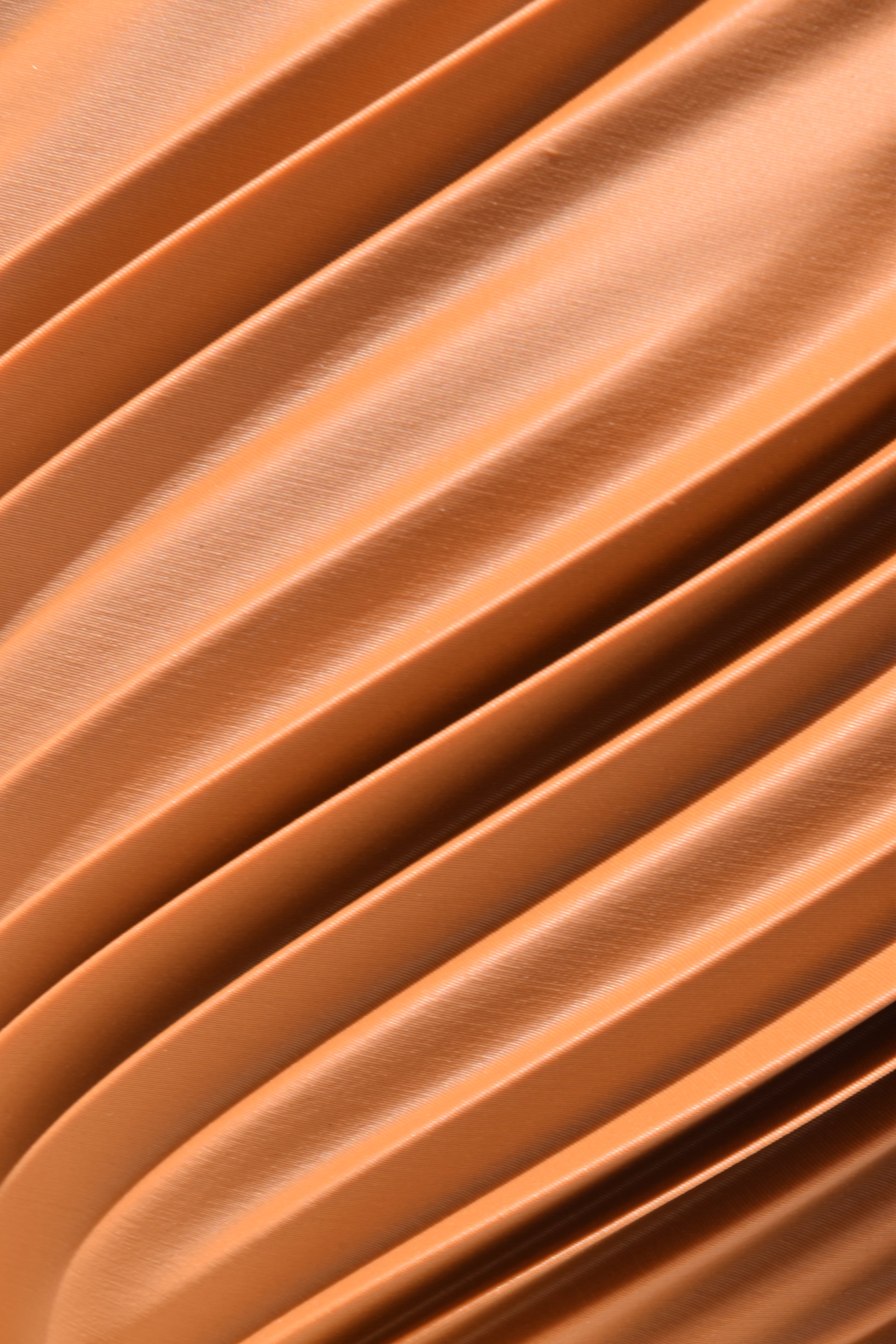 Detailaufnahme einer 3D-gedruckten Oberfläche in einem warmen Terrakotta (Lehmbraun). Die geschwungenen und spiralförmigen  Rillen verlaufen diagonal über das Bild und erzeugen eine fließende, organische Struktur.