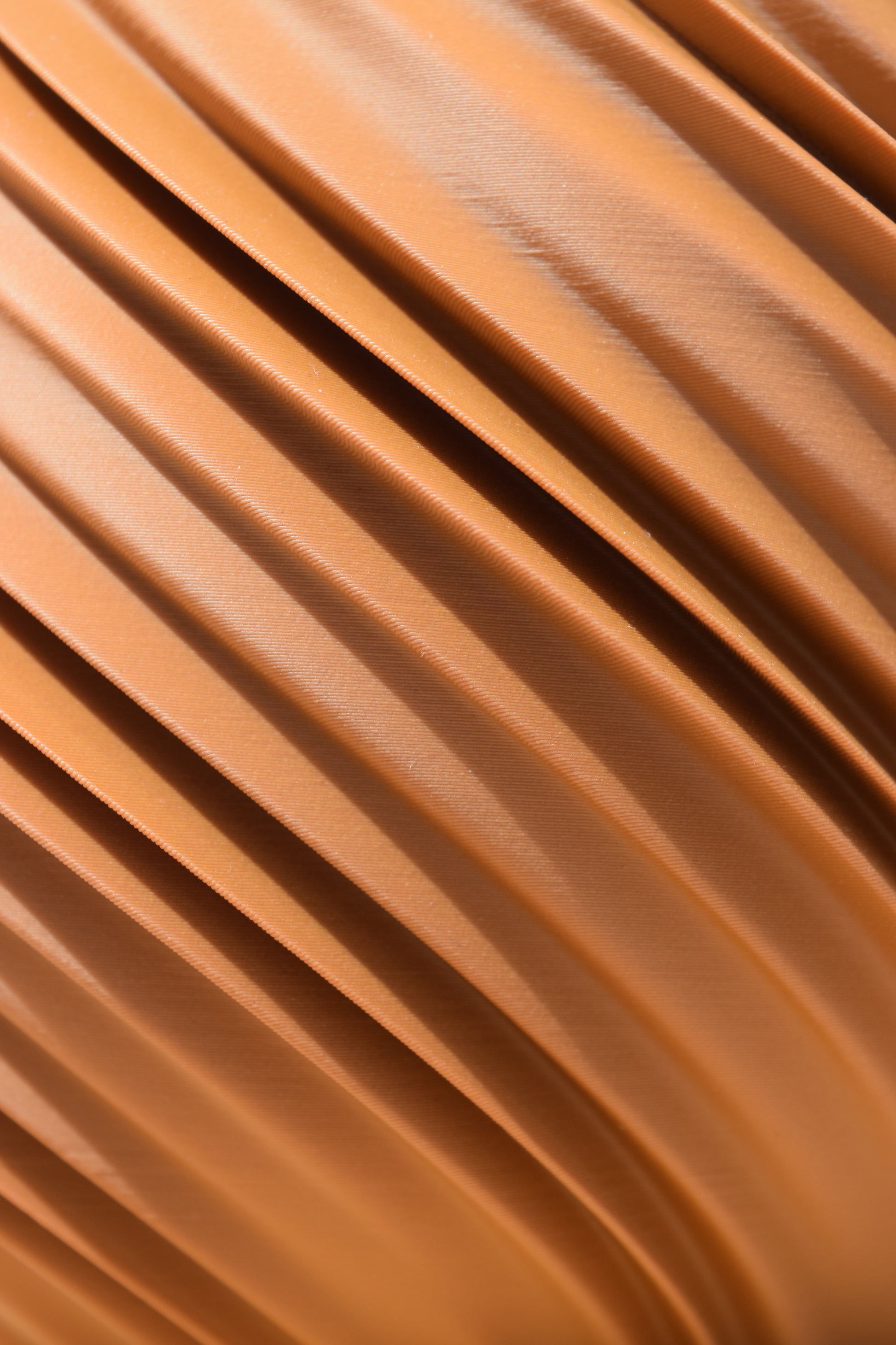 Detailaufnahme einer 3D-gedruckten Oberfläche in einem warmen Terrakotta (Lehmbraun). Die geschwungenen und spiralförmigen  Rillen verlaufen diagonal über das Bild und erzeugen eine fließende, organische Struktur.