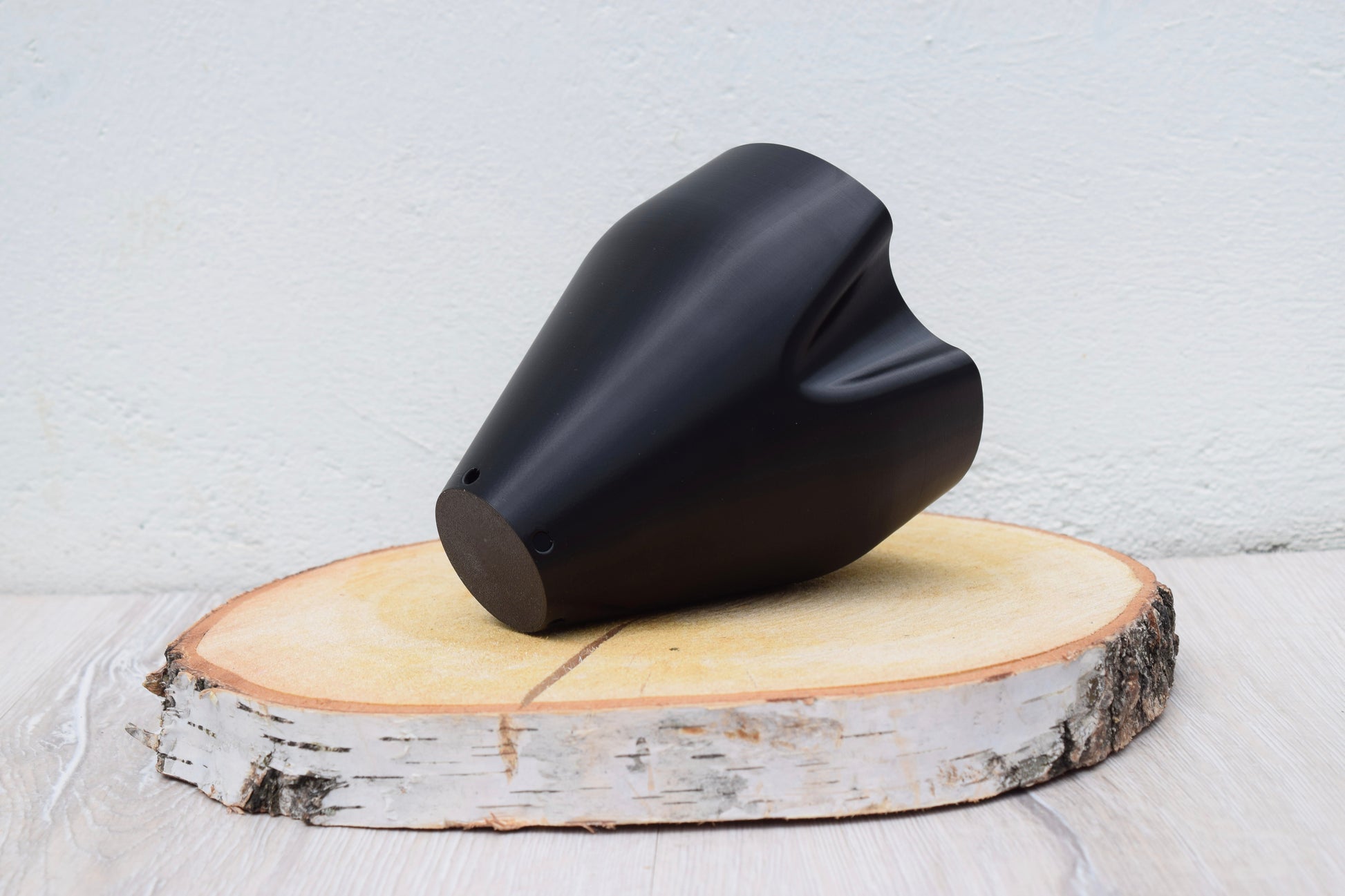 Ein schwarzes 3D-gedruckter Innentopf mit weichen, fließenden Konturen und moderner Gestaltung. In der Farbe Schwarz. Der Innentopf steht auf einer  runden Holzscheibe und hat einen schlichten hellen Hintergrund.