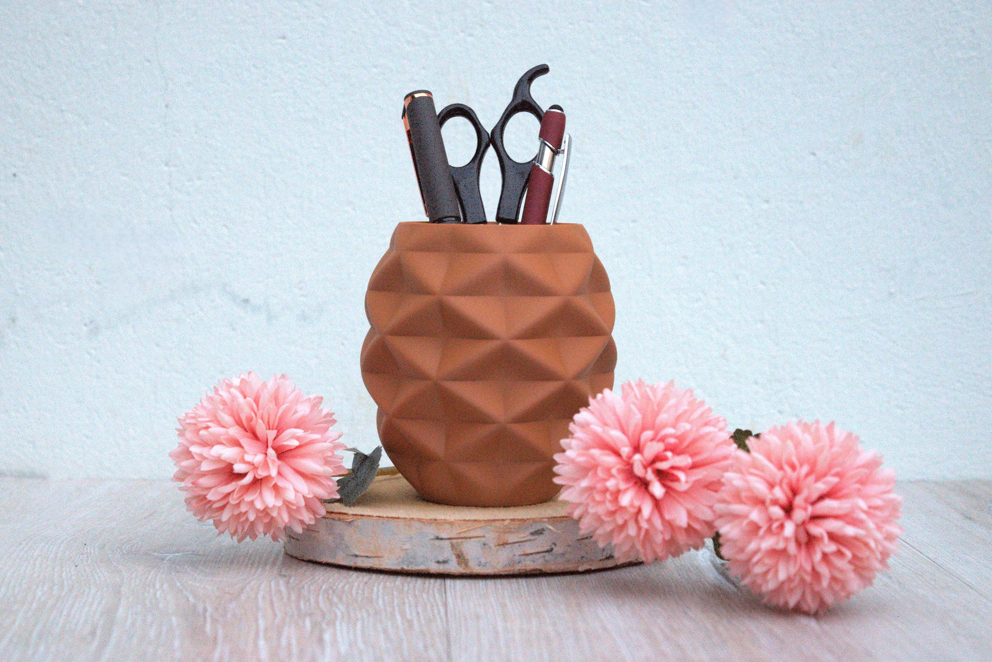 Geometrische, runde , Terrakotta (Lehmbraun) Stiftehalter mit scharfem Rautenmuster, der einen schwarzen Stift und eine rote und schwarze Schere hält, mit zwei flauschigen, pinken Deko-Blumen auf einer hölzernen Unterlage.

Verschönere dein Büro oder Schreibtisch.
Besteht aus PLA Wood.
